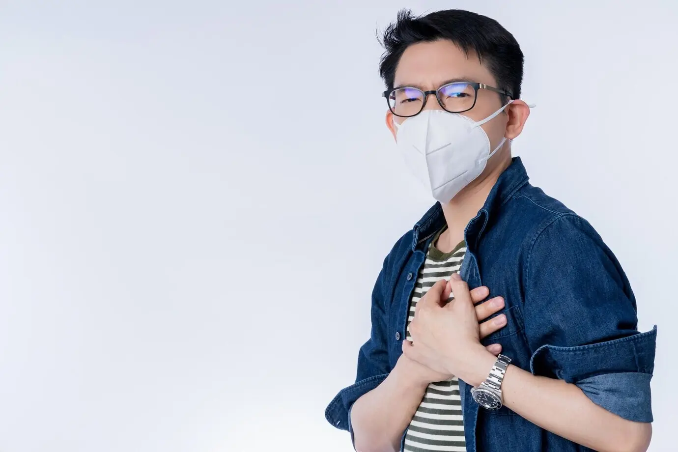 Primer plano de un joven empresario asiático con mascarilla contra la contaminación, haciendo un gesto que expresa enfermedad y mala salud por el problema del aire con PM2.5 en la ciudad.
